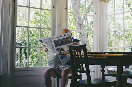 man reading newspaper sitting beside table and glass window thumbnail