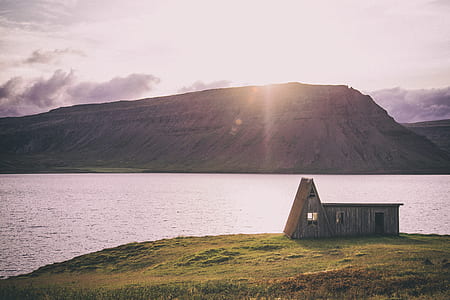 photo of brown house near body of water with mountain in vicinity thumbnail