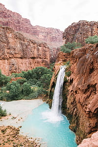 rock cliff waterfall surrounded with mountains and tree thumbnail