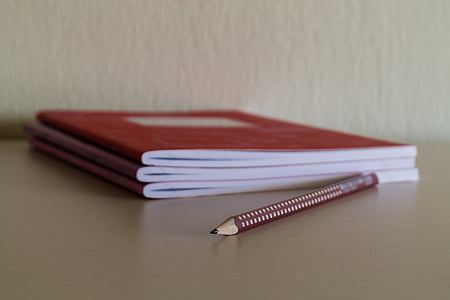 red and beige pencil beside three red notebooks thumbnail