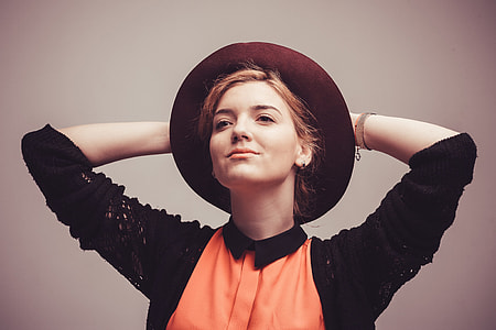 photography of woman in black cardigan and orange shirt wearing hat thumbnail