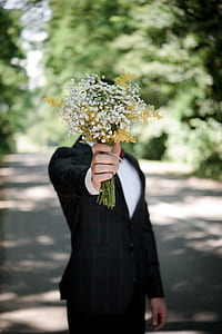 man in black and white tuxedo holding white and yellow flower bouquet in front of his face selective-focus photography thumbnail