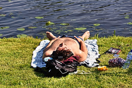 man lying on grass near lake thumbnail