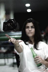 woman holding green bottle throwing black Canon DSLR camera thumbnail