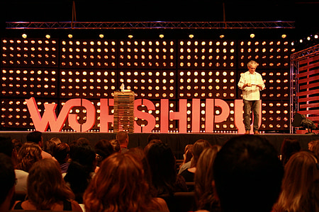 man standing on platform stage in front of crowd thumbnail