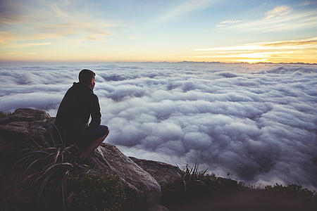 man sitting on rock facing cloudy during daytime thumbnail