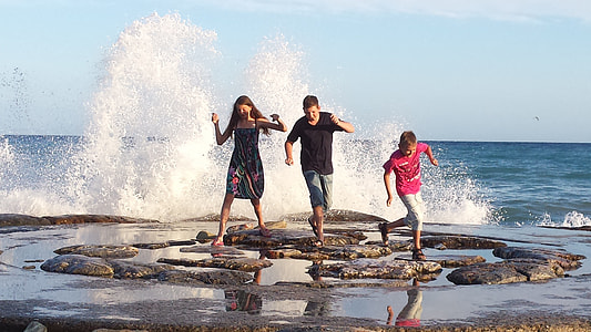 two girl and one boy running on rock near ocean during daytime thumbnail
