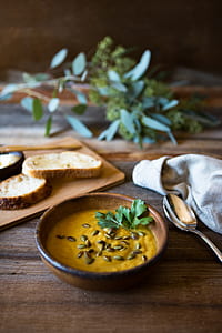 creamy soup in round brown bowl beside gray steel spoon on brown table thumbnail
