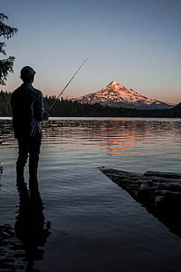 man fishing on lake facing snowy mountain thumbnail