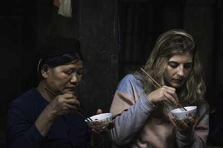 two women eating on bowl using chopsticks thumbnail