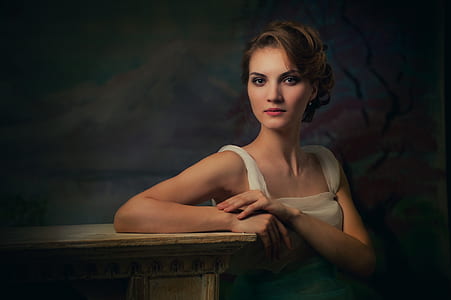 woman in white top leaning on brown wooden table thumbnail