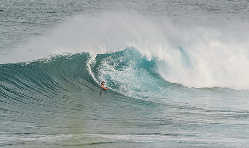 person surfing with orange surf board at day time thumbnail