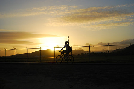 silhouette of woman riding a bike with view of sunset thumbnail