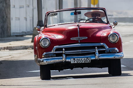 person driving classic red vehicle on road thumbnail