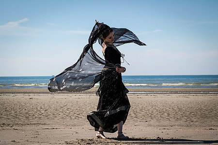 woman in black long dress holding scarf standing on seashore thumbnail