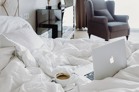 Woman working on a laptop while enjoying a breakfast coffee and chocolate in bed thumbnail