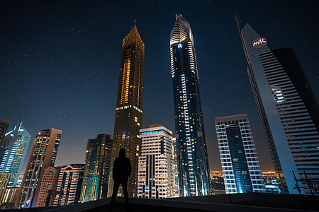 Man Standing in Assorted Building String Light during Night Time thumbnail
