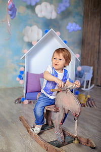 toddler riding rocking horse beside white wooden dollhouse thumbnail