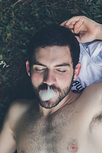 topless man lying on grass with smoke on mouth in aerial shot thumbnail