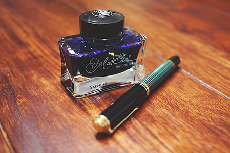 Edelstein Sapphire bottle beside black and green pen on brown wooden surface thumbnail