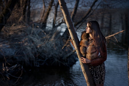 woman holding log standing beside body of water photo thumbnail