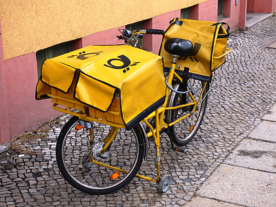 yellow commuter bike with bags parked beside wall thumbnail