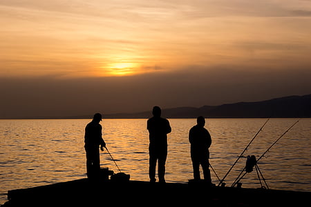 silhouette of three person standing and fishing at golden hour thumbnail