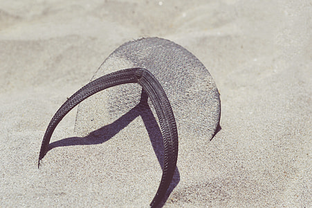 unpaired brown rubber flip-flop half buried on beige sand during daytime thumbnail