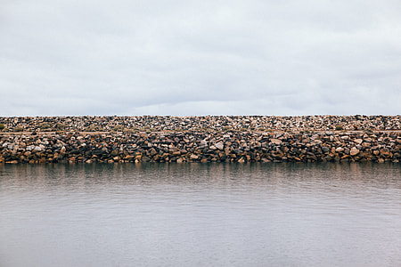 stack of rocks in front of body of water under white clouds thumbnail