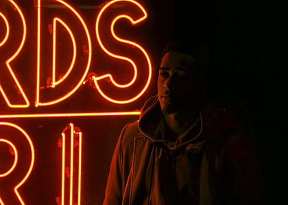 man standing in front of red neon signage during nighttime photo thumbnail