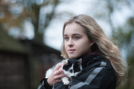 woman carrying white and black kitten near tree thumbnail