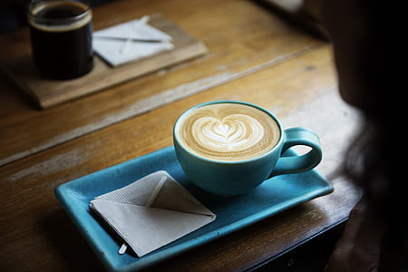 blue ceramic teacup with beverage foam art on brown wooden table closeup photography thumbnail