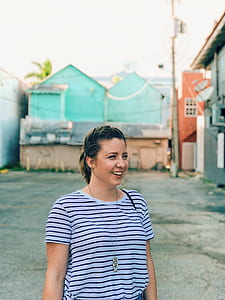 smiling woman in black and white striped crew-neck shirt stands near green house during daytime thumbnail