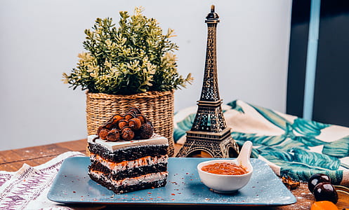 flat lay photography of piece of cake and sauce on plate beside Eiffel Tower miniature on table thumbnail