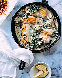 salmon fish with coconut milk in black skillet iron near slice of lemons in white saucer thumbnail