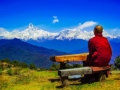 man wearing red robe sitting on black bench looking at snow covered mountain thumbnail