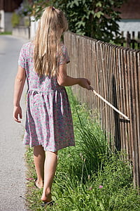 girl holding stick walking beside fence thumbnail