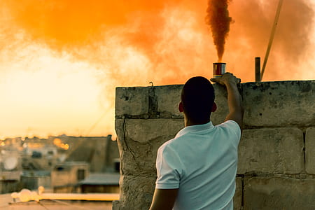 man standing beside concrete wall while holding can with smoke inside thumbnail