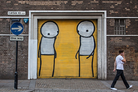 A man walks past a one-way sign and street art background in Shoreditch, East London thumbnail