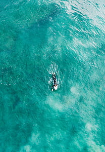 aerial photography of person lying on white surf board on clear blue water during daytime thumbnail