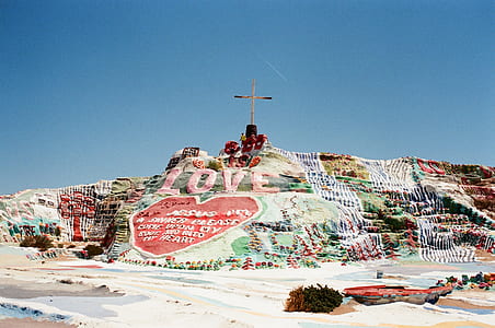landscape photography of painted rock formation with cross on peak thumbnail