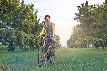 Young Farmer In Gray Sleeveless Vest Riding A Bicycle In The Meadow thumbnail