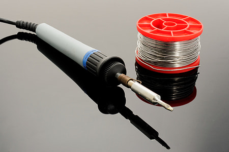 gray soldering iron and soldering lead spool on gray surface thumbnail