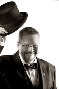grayscale photo of man wearing notched lapel suit jacket and holding fedora hat thumbnail