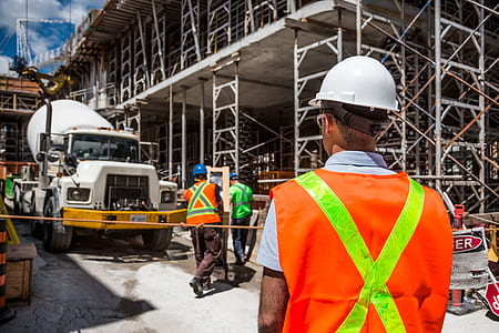 man wearing white hard hat and reflector vest standing in front of gray metal building with white truck cement mixer at daytime thumbnail