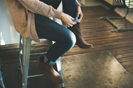 person folding edge of denim pants while sitting on grey stool thumbnail