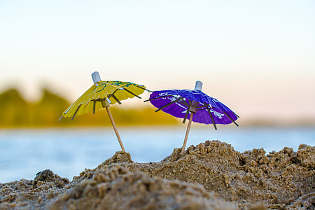 green and blue miniature umbrella stick on sand during day time thumbnail