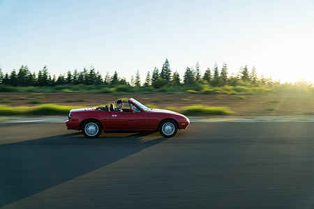 person driving red convertible coupe running on concrete road thumbnail