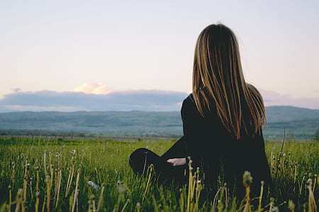 Woman Wearing Black Long Sleeved Shirt Sitting on Green Grass Field Near Mountain Under Cloudy Sky thumbnail