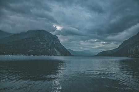 body of water near mountain under white clouds at daytime thumbnail